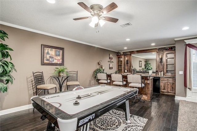 game room featuring dark hardwood / wood-style floors, ceiling fan, ornamental molding, and bar