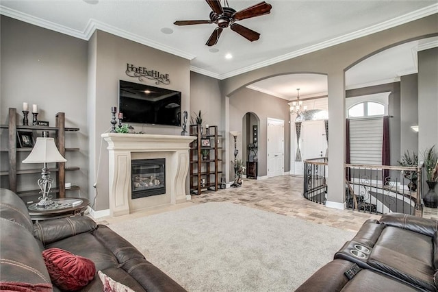 living room with arched walkways, ceiling fan with notable chandelier, a fireplace with flush hearth, baseboards, and ornamental molding