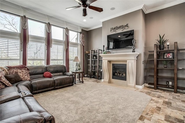 living room featuring ceiling fan, stone finish floor, crown molding, and a glass covered fireplace