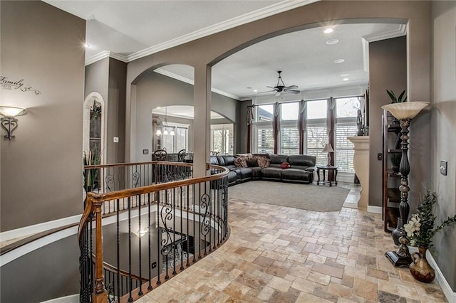 hall featuring baseboards, arched walkways, an upstairs landing, crown molding, and stone tile flooring