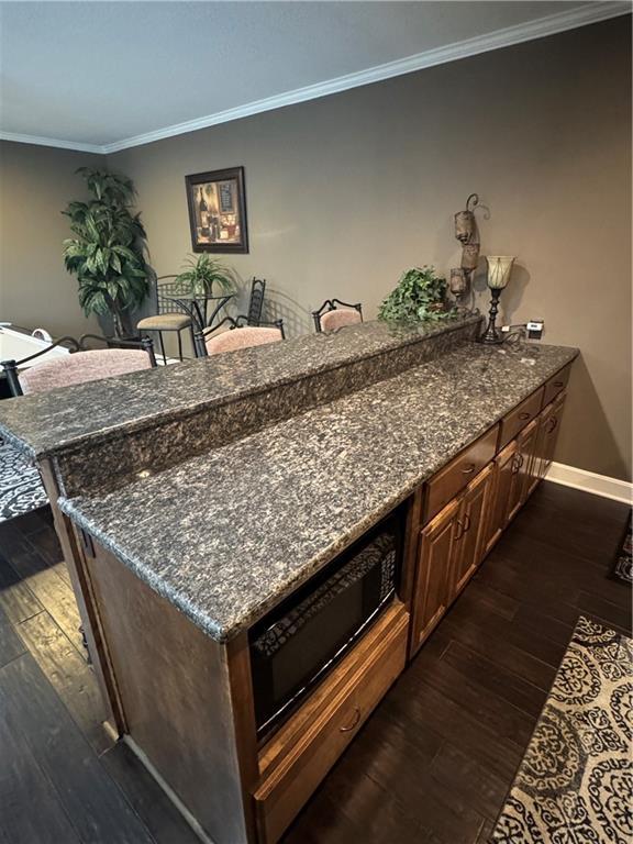 kitchen with dark wood-style flooring, crown molding, dark stone countertops, a peninsula, and baseboards