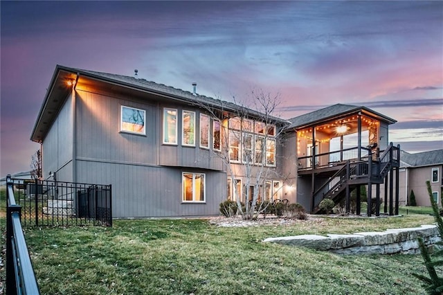 back of property at dusk with a yard, stairway, a wooden deck, and fence