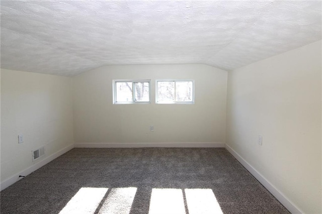 additional living space featuring dark carpet, vaulted ceiling, and a textured ceiling