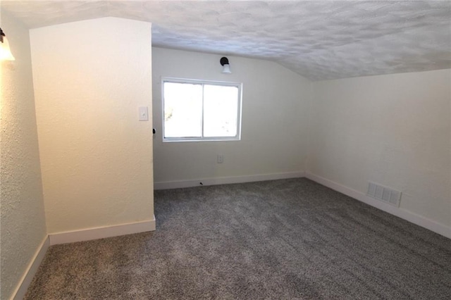 spare room featuring vaulted ceiling, a textured ceiling, and dark colored carpet