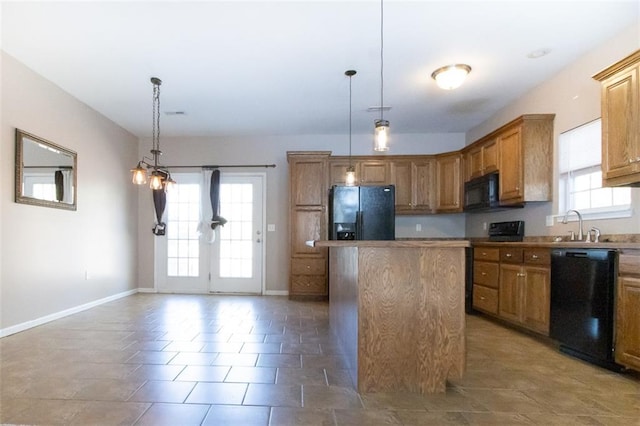 kitchen with hanging light fixtures, dark tile patterned floors, black appliances, sink, and a center island