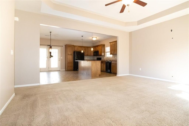 unfurnished living room featuring sink, ceiling fan, light colored carpet, and a raised ceiling