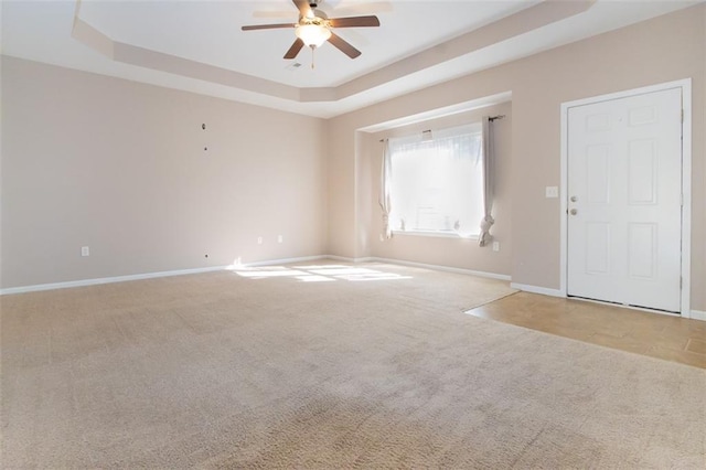 spare room featuring ceiling fan, light colored carpet, and a raised ceiling