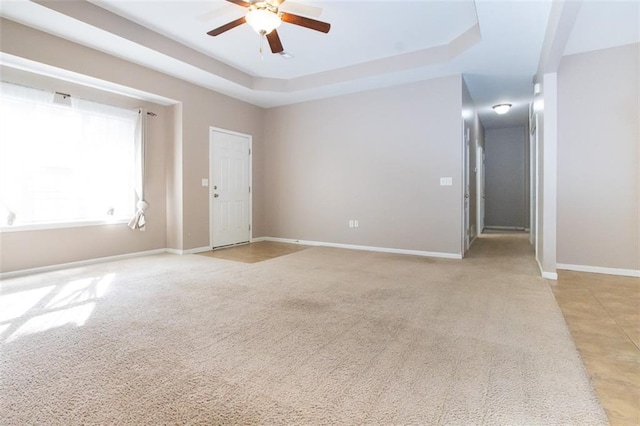 spare room featuring ceiling fan, light colored carpet, and a raised ceiling