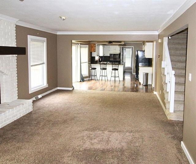 unfurnished living room with a brick fireplace, ornamental molding, and dark colored carpet