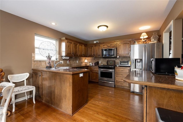 kitchen with backsplash, kitchen peninsula, dark hardwood / wood-style flooring, and stainless steel appliances