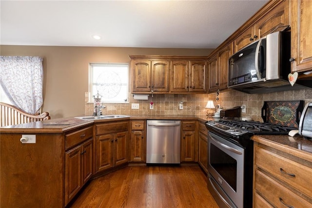 kitchen featuring backsplash, sink, appliances with stainless steel finishes, dark hardwood / wood-style flooring, and kitchen peninsula