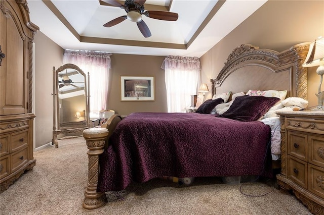 carpeted bedroom with a raised ceiling and ceiling fan