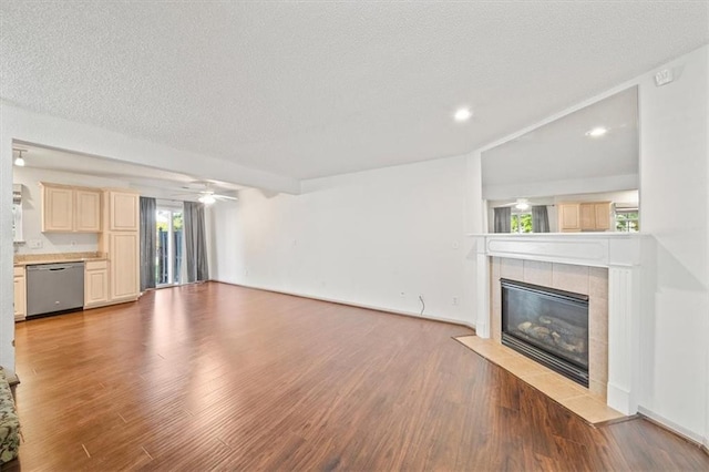 unfurnished living room featuring a textured ceiling, light hardwood / wood-style floors, ceiling fan, and a tiled fireplace