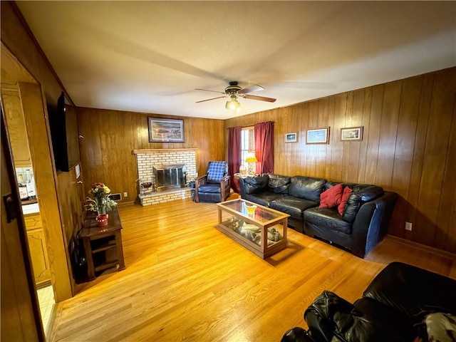 living room with wooden walls, a brick fireplace, wood-type flooring, and ceiling fan