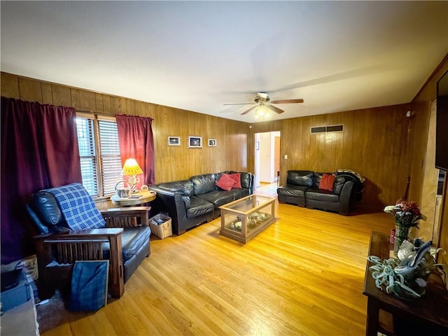 living room with wooden walls, light wood-type flooring, and ceiling fan