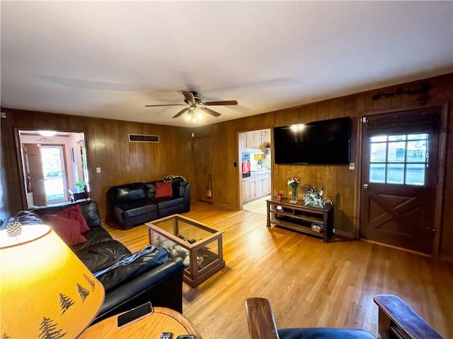 living room with light hardwood / wood-style floors, wooden walls, and ceiling fan