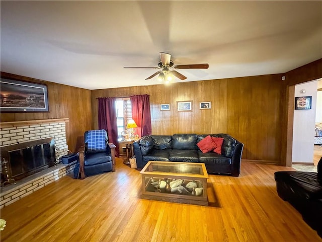 living room with wooden walls, light hardwood / wood-style flooring, a fireplace, and ceiling fan