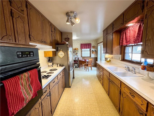 kitchen with stainless steel fridge, tasteful backsplash, white gas stovetop, black oven, and sink