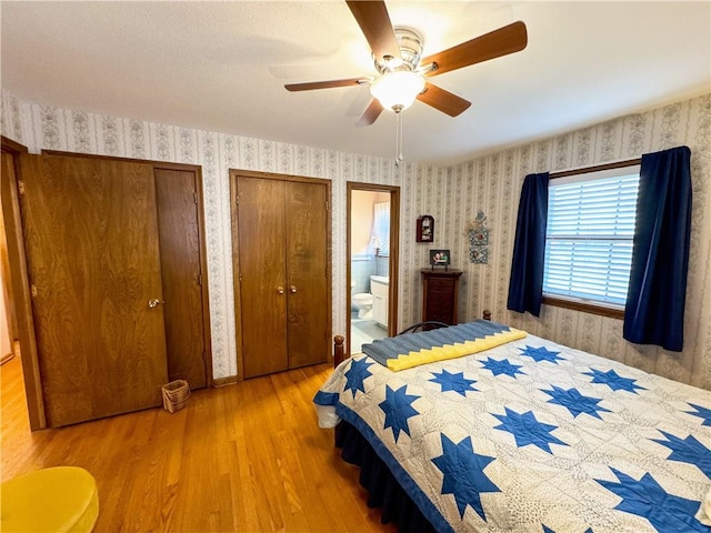 bedroom with hardwood / wood-style flooring, connected bathroom, two closets, and ceiling fan