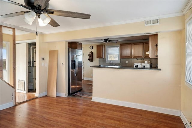 kitchen featuring kitchen peninsula, ornamental molding, backsplash, dark wood-type flooring, and stainless steel fridge