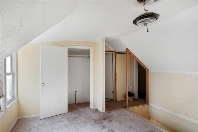 unfurnished bedroom featuring a closet, lofted ceiling, a textured ceiling, and light carpet