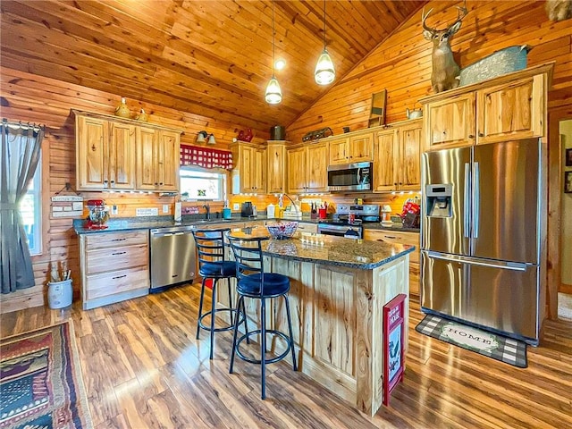 kitchen featuring high vaulted ceiling, wood walls, pendant lighting, a kitchen island, and appliances with stainless steel finishes