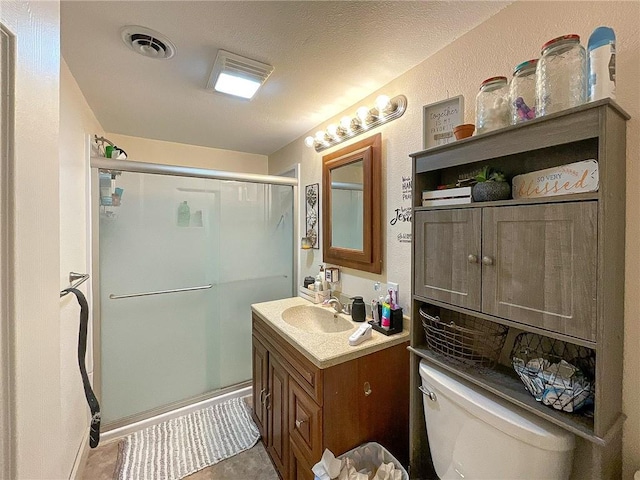 bathroom featuring vanity, toilet, a shower with shower door, and a textured ceiling