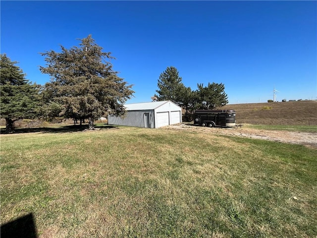 view of yard featuring a rural view, a garage, and an outbuilding