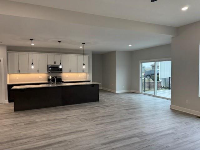 kitchen with sink, decorative light fixtures, a center island with sink, light hardwood / wood-style floors, and white cabinetry