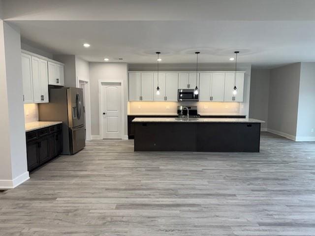 kitchen featuring a kitchen island with sink, white cabinets, pendant lighting, and appliances with stainless steel finishes