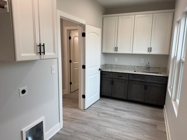 kitchen featuring white cabinets, light wood-type flooring, light stone counters, and sink