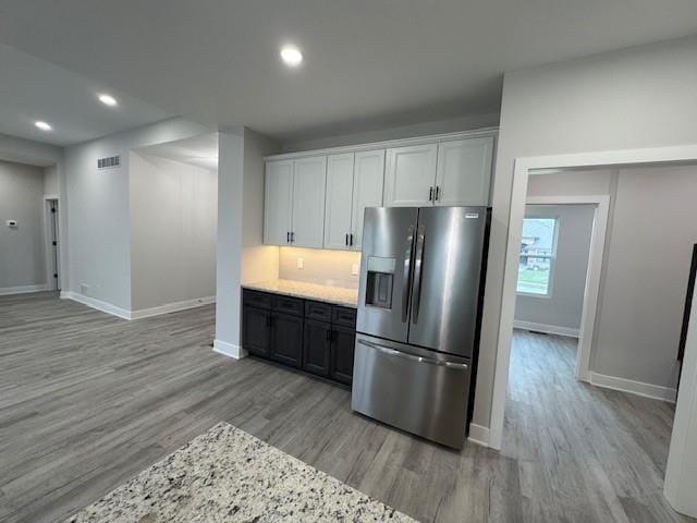 kitchen with tasteful backsplash, white cabinetry, stainless steel refrigerator with ice dispenser, and light hardwood / wood-style flooring