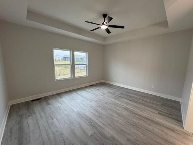 unfurnished room featuring ceiling fan, light hardwood / wood-style floors, and a raised ceiling