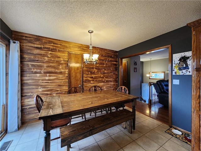 dining room with light tile patterned flooring, a textured ceiling, a notable chandelier, and wooden walls