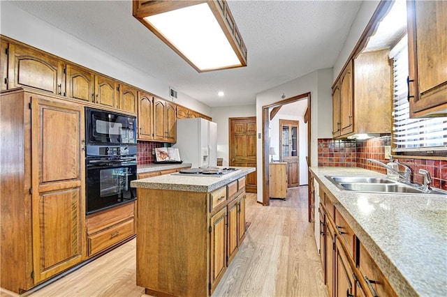 kitchen with a center island, black appliances, sink, light wood-type flooring, and tasteful backsplash