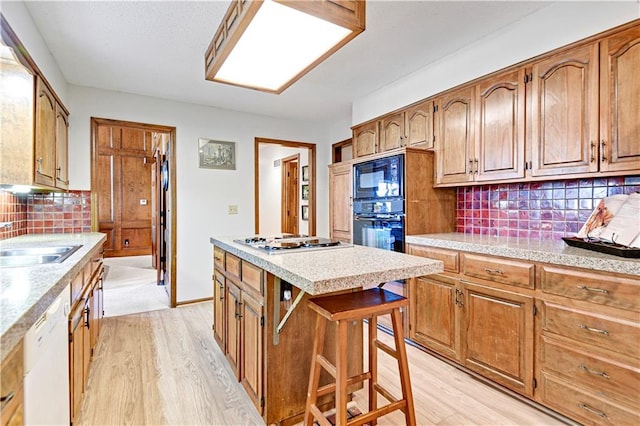 kitchen with light hardwood / wood-style floors, a kitchen bar, decorative backsplash, a kitchen island, and black appliances