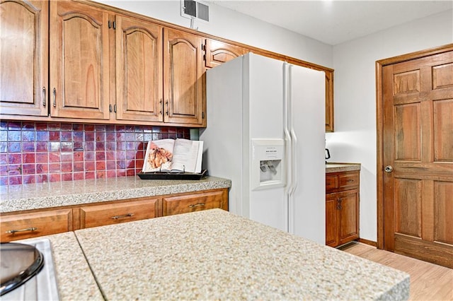 kitchen with light wood-type flooring, tasteful backsplash, and white fridge with ice dispenser