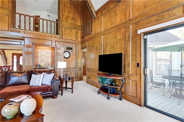 carpeted living room with wood walls, plenty of natural light, and a high ceiling