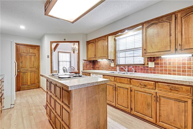 kitchen with sink, light wood-type flooring, tasteful backsplash, a kitchen island, and stainless steel gas cooktop