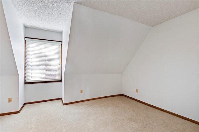 additional living space with lofted ceiling, light carpet, and a textured ceiling