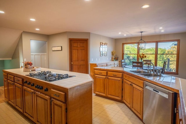 kitchen featuring an island with sink, stainless steel appliances, sink, tile counters, and decorative light fixtures