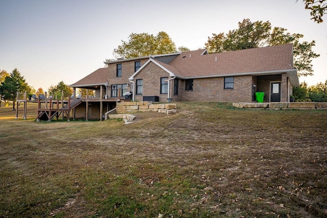 back house at dusk featuring a deck and a lawn