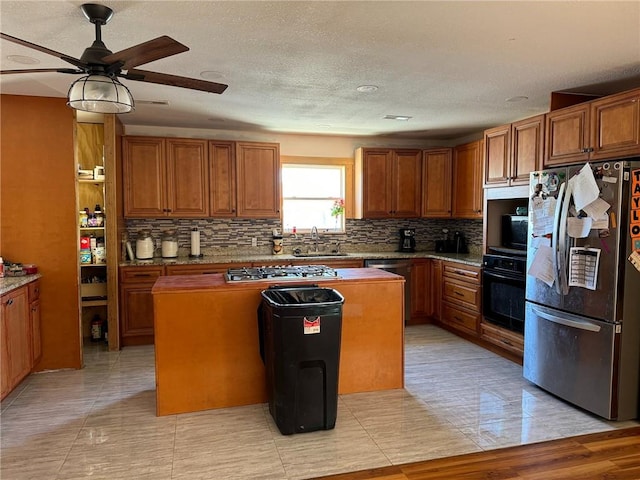 kitchen featuring stainless steel appliances, sink, a center island, ceiling fan, and backsplash