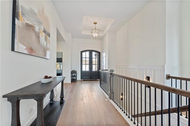 hallway featuring french doors, a notable chandelier, a tray ceiling, and hardwood / wood-style floors