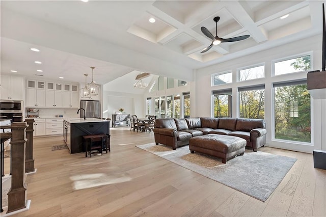 living room with a high ceiling, beam ceiling, ceiling fan with notable chandelier, and light wood-type flooring