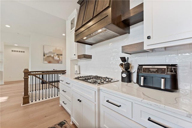 kitchen featuring stainless steel gas cooktop, premium range hood, white cabinets, and light wood-type flooring