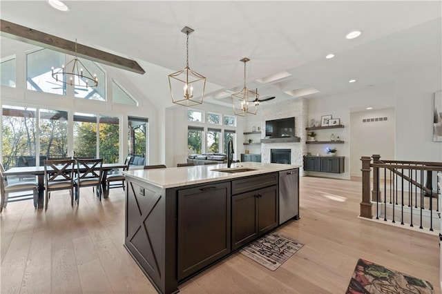 kitchen with light wood-type flooring, an island with sink, a fireplace, decorative light fixtures, and stainless steel dishwasher