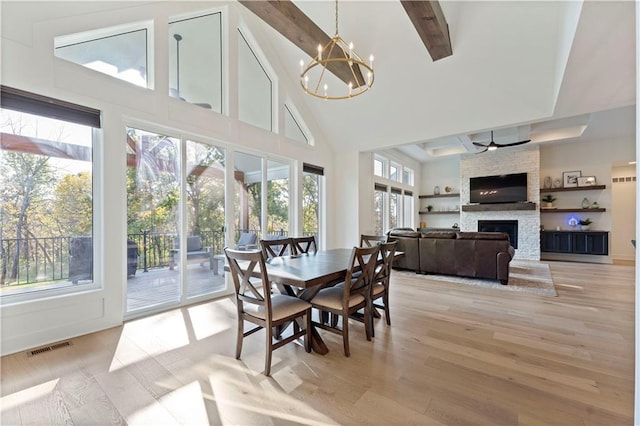 dining room featuring a stone fireplace, light hardwood / wood-style floors, beam ceiling, high vaulted ceiling, and an inviting chandelier