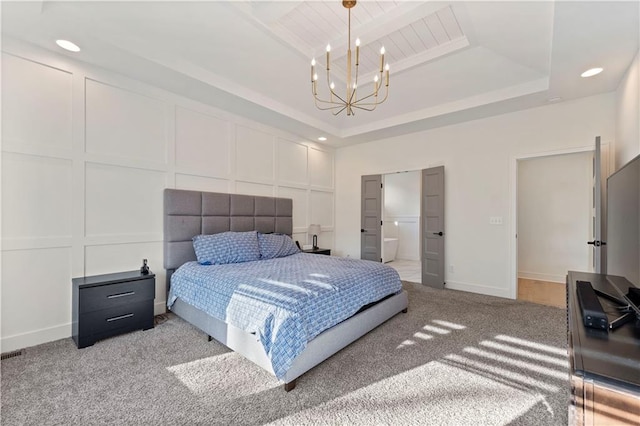 bedroom featuring an inviting chandelier, ensuite bathroom, a tray ceiling, and carpet