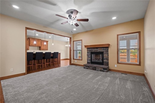 living room with dark colored carpet, a stone fireplace, and ceiling fan